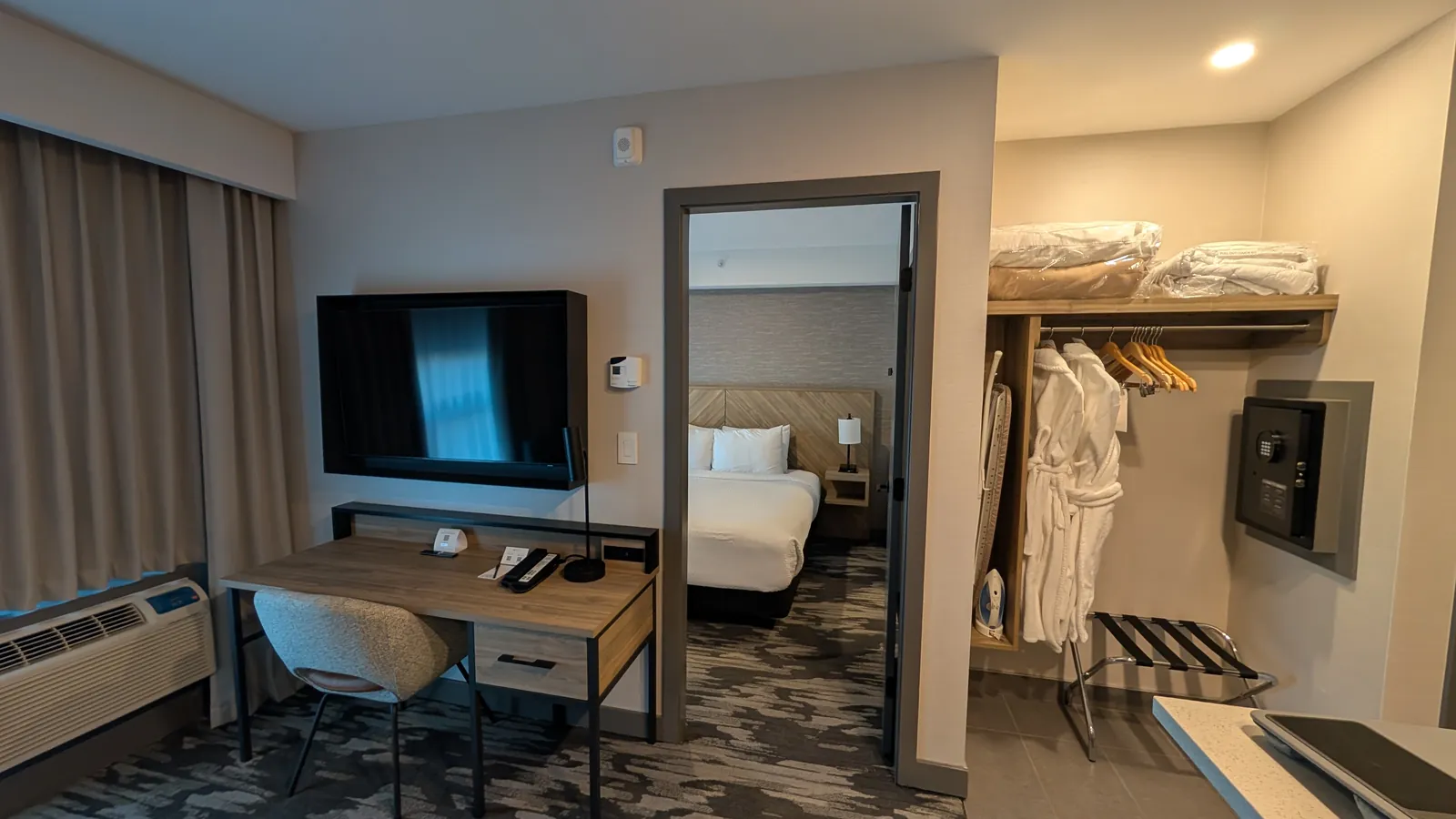 Living room desk and the open closet with robes, safe, and luggage rack