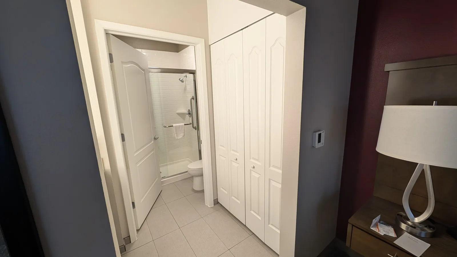 The open bathroom door, toilet, and glass shower enclosure show the narrow space for closing the door